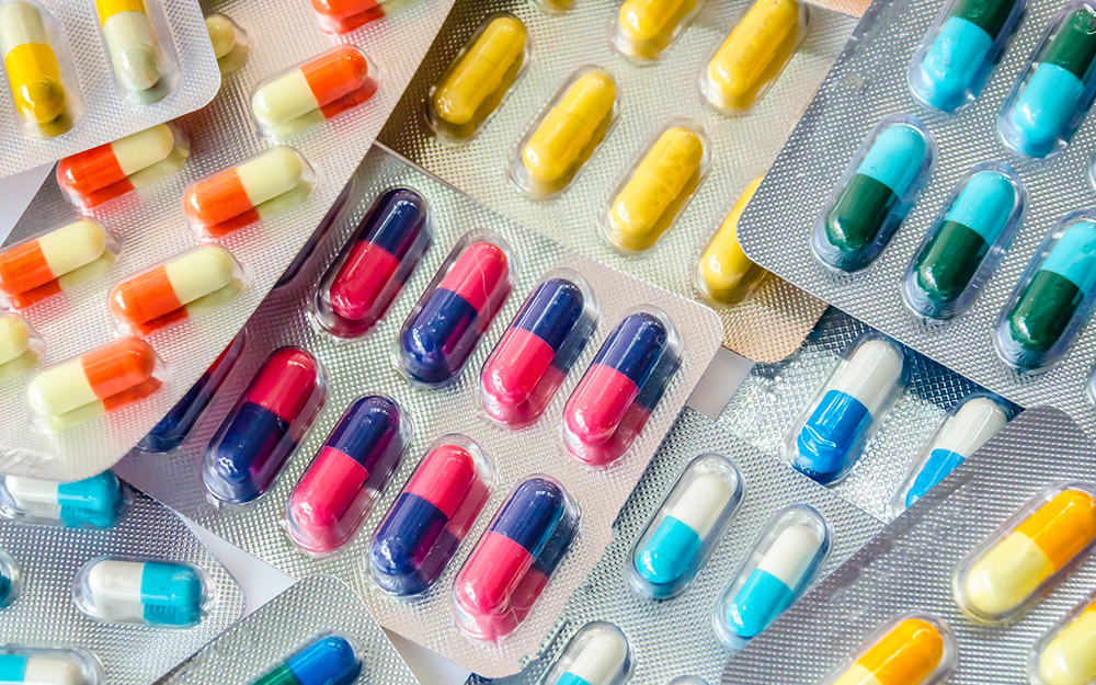 A close up image of plastic packaged pills next to each other. The packages of pills are uniform, and the color combinations are pink and dark blue, light blue and white, and solid yellow.