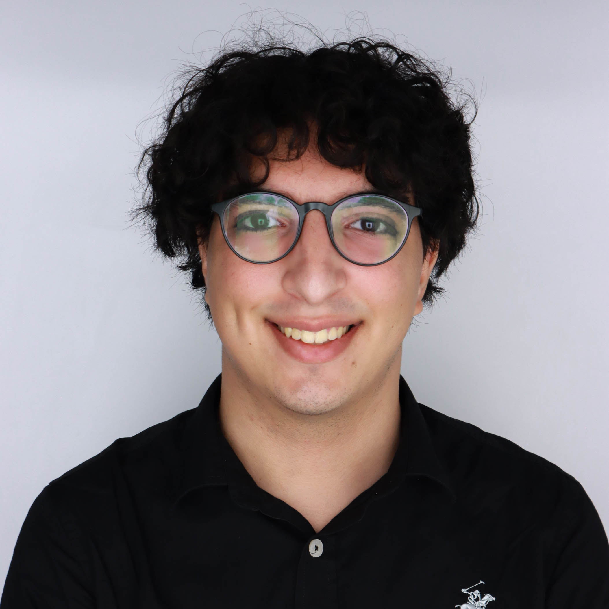 A forwarding facing headshot of a male team member. He has black hair, tan skin, and is smiling wide at the camera.